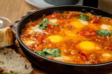 Traditional oriental cuisine. Arabic dish Shakshuka. Turkish breakfast, fried eggs, tomato sauce, peppers, cilantro and 2 pieces of baguette.