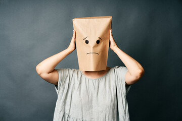 Upset woman with a paper bag on head touching temples, suffering from strong tension headache