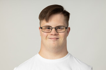 A smiling young man with cerebral palsy in glasses and a white T-shirt poses for the camera. World...