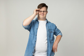 A smiling young man with cerebral palsy in glasses, jeans and a white T-shirt poses for the camera....