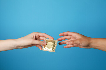 A condom is passed from hand to hand on a blue background - obrazy, fototapety, plakaty