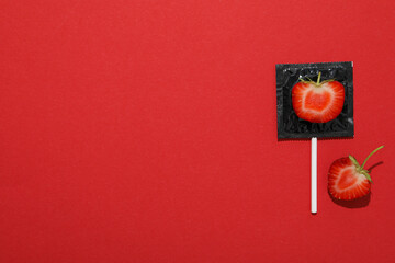 Black condom with strawberry on red background, place for text