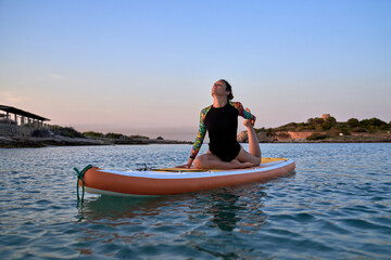 Sporty woman practicing yoga on SUP board