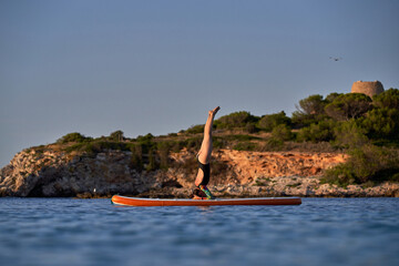 Sportswoman taking Supported Headstand pose on paddleboard in se