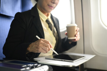 Mature businesswoman sitting at her seat in airplane and using digital tablet.