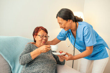 Senior Woman Sitting In Chair And Laughing With Nurse In Retirement Home. Female Support Worker Visits Senior Woman At Home. Senior woman and home caregiver