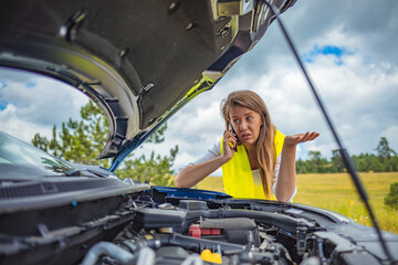 Woman on the road trying to fix the broken car, and calling for help on her mobile phone. Woman having problem with her car, it stopped on the street. She is calling for help