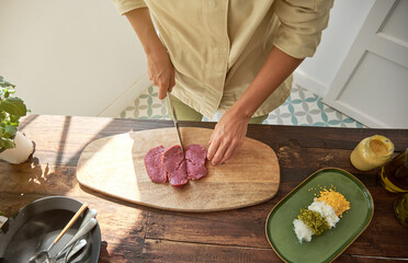 Crop woman slicing meat on wooden board