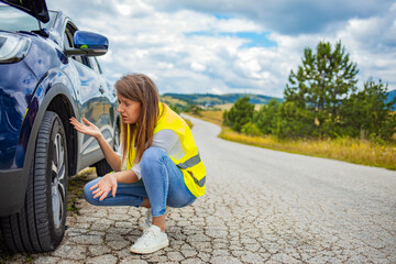 Young brunette woman standing infront of the car, trying to fix the problem. Casual brown hair women in the city with a flat tire frustrated.  Woman changing a wheel after a car breakdown 