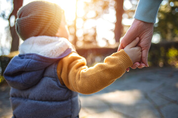 Close up of mother and a child hands at the sunset. A parent holds the hand of a small boy in the sunset. Mother holding her little boys hand walking down the street - obrazy, fototapety, plakaty