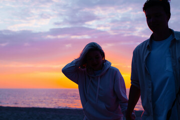 Couple of young lovers girlfriend and boyfriend holding hands walking on seashore at sunset, copy space