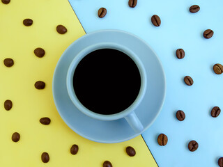 Creative layout made of blue coffee cup and coffee beans against yellow and blue background. Flat lay, copy space. Good morning. Coffee art. Minimal concept.