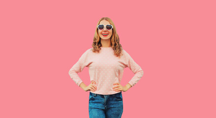 Portrait of beautiful young woman posing wearing white heart shaped sunglasses, sweater on pink studio background