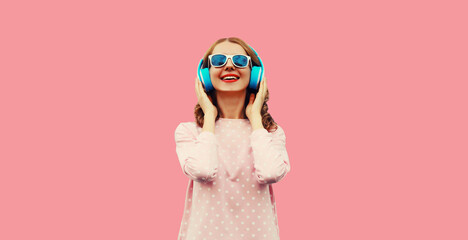 Portrait of happy smiling young woman listening to music in wireless headphones on pink background