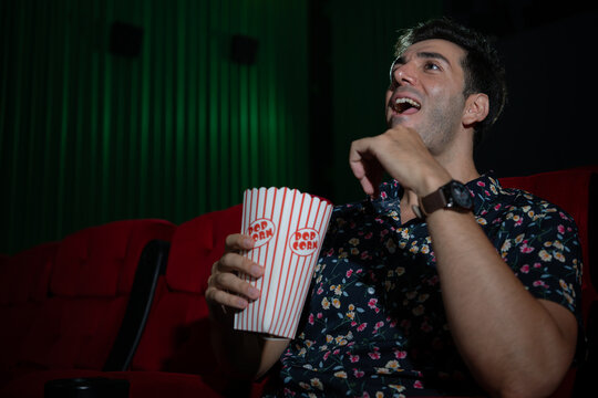 Young man watching movie and eating popcorn while sitting on red couch