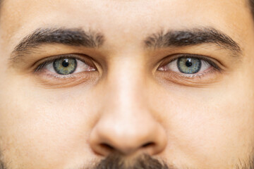 Extreme close-up macro portrait of face. Young adult handsome bearded man's eyes looking at camera. Gray green eyes of guy male boy. Caucasian man opening blinking eyes, smiling. Laser correction