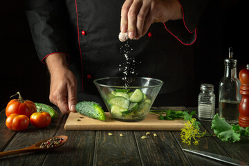 Cooking vegetable salad by the hands of the chef. Adding Salt to Cucumber and Tomato Salad