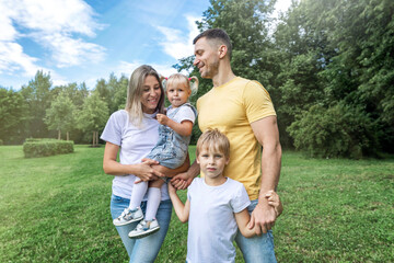 Happy family with children in the park on a sunny day. Mom, dad and little daughter and son in jeans and white t-shirts laugh and hug. Love and tenderness.