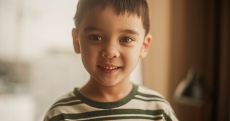 Portrait of a Little Cute Asian Boy Looking at the Camera and Smiling. Naturally Lit Portrait of a Cheerful Male Child Standing Near a Window in his Home. Eyes Full of Innocence and Wonder.