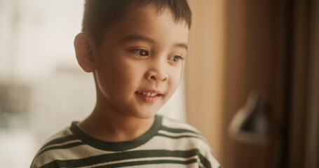 Portrait of a Little Cute Asian Boy Smiling At Home In His Sunny Room. Naturally Lit Portrait of a Cheerful Male Child Standing Near a Window in his Home. Eyes Full of Innocence and Wonder.