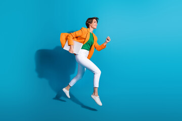 Fototapeta na wymiar Profile side photo of excited cheerful active lady wear stylish orange clothes go fast empty space isolated on blue color background