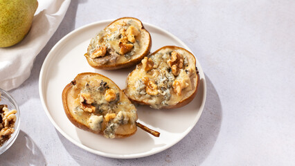 Baked pears with blue cheese, walnuts and honey on white plate and light background