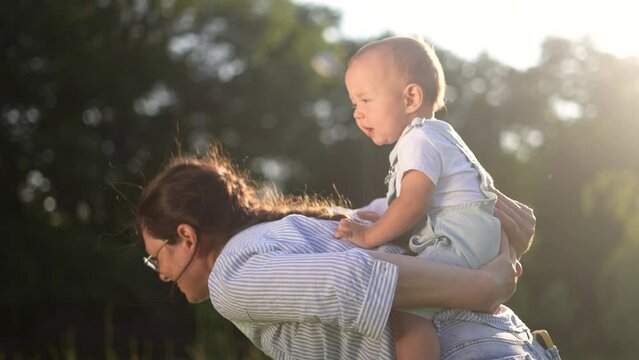 mother plays with baby son nature park. happy family kid dream concept. mom rolls her son baby on her back in nature in the summer in the park playing. child having fun with lifestyle mom outdoors