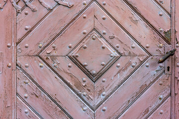Close-up of an old, church wooden door with a handle and keyhole. The door is made from planks of wood that have been weathered by the elements over time, giving it a rustic look.