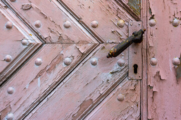 Close-up of an old, wooden door with a handle and keyhole. The door is made from planks of wood that have been weathered by the elements over time, giving it a rustic look.