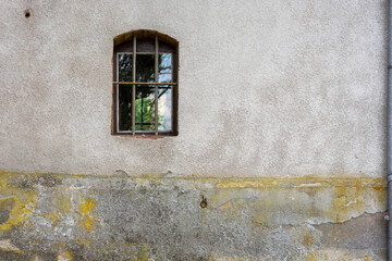 A small arched window protected by a lattice on a solid concrete wall that is weathered and faded.