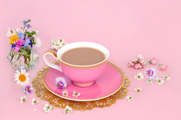 Afternoon tea with Spring flowers and wildflowers in a vase and scattered. Luxury tea cup on gold doily on pink background.