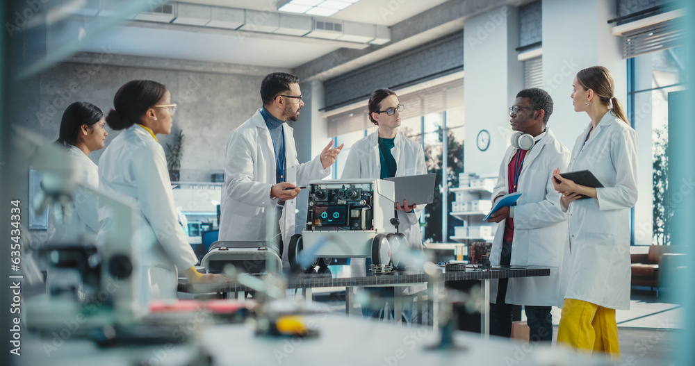 Poster Diverse Team of Industrial Robotics Specialists Gathered Around a Table With a Mobile Robot. Engineers In Lab Coats Discussing an Automated AI Robotic Delivery Assistant, Using Laptop, Tablet