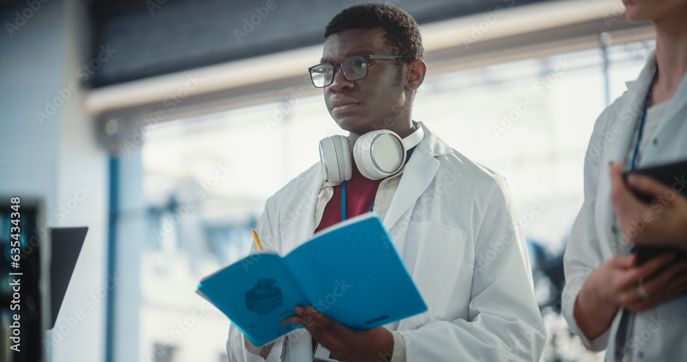 Poster portrait of a young black male engineering student asking questions, taking notes in a laboratory. l