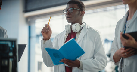 Portrait of a Young Black Male Engineering Student Asking Questions and Taking Notes in a Laboratory. Lab Assistant in a Meeting Showing Initiative and Giving Ideas, Brainstorming with his Team