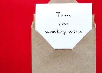 Envelope on red background with note written TAME YOUR MONKEY MIND, Buddhism mindfulness practice...
