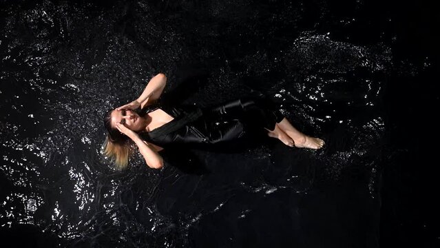 Seductive pretty wet young lady squeezes wet clothes, top standing under rain shower slow motion isolated on black studio background. Aqua studio 4k video slow motion 120 fps raw footage