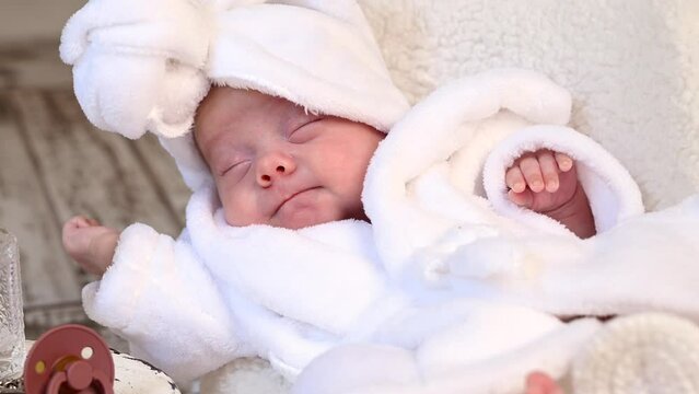 Sleeping newborn beautiful cute baby girl or boy during first week of life. 4k slow motion raw video. Happy Family morning concept. Small baby at white chair in white bathroom coat with towel on head 