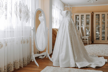 Fototapeta na wymiar white wedding dress with long train near mirror in room with home interior