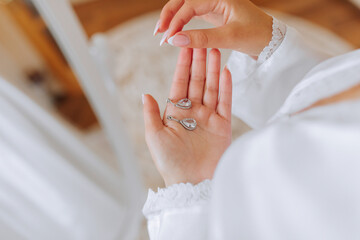 Obraz premium The bride holds in her hands and shows her earrings with precious stones, close-up. Morning of the bride. The wedding day.