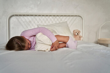Obraz na płótnie Canvas Elementary age girl lying on bed with head hidden in legs