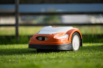 robotic lawn mower at work in a fenced yard with freshly cut green lush grass
