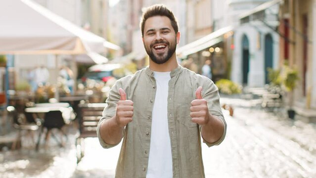 Like. Happy bearded young man looking approvingly at camera showing thumbs up, like sign positive something good positive feedback. Guy standing in urban city sunshine street. Town lifestyles outdoors