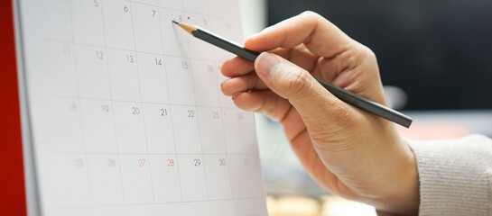 close up on employee man hand with pencil writing on calendar to mark date and specify time of...