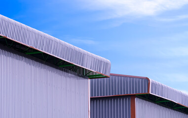 Fototapeta premium Gray corrugated steel wall with roof eaves of two warehouse buildings against blue sky background in perspective side view