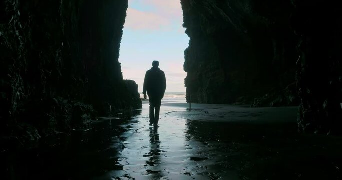 Aerial: Man walking out of a cave into the light. 