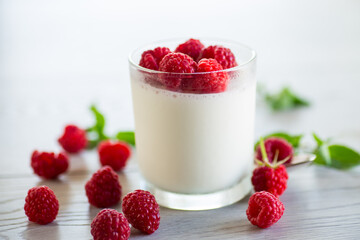 Cooked homemade yogurt with ripe red raspberries in a glass.