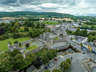 Aerial view of Cahir castle and town in Ireland with Tower House, outer castle, circular, rectangular towers, banquette hall, guarding the crossing on the River Suir with a waterfall and golf course