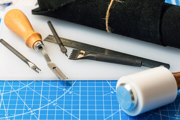 Leather work tools and leather roll piece on the cutting mat close up background.