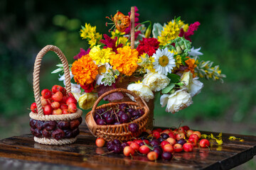 Fototapeta na wymiar Artistic still life with a bouquet of garden flowers and cherries in a basket on a wooden table against a dark background