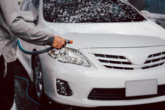 Unidentified man washing a car with high pressure foam.